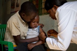 A health worker with GAVI vaccinates a . young boy being held by his brother against measles and rubella in Tanzania